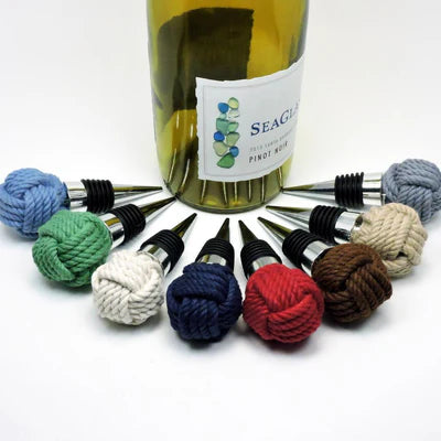 Colorful knot shaped wine bottle stoppers in front of a bottle of wine