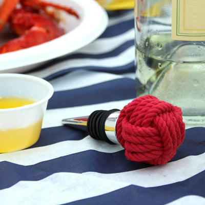 Red knot-shaped bottle stopper on a table with food and drinks in the background